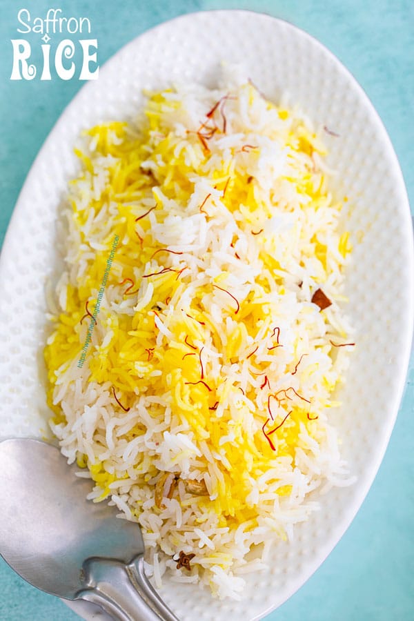 Top view of a white oval plate with saffron rice and a stainless steel rice server on the side