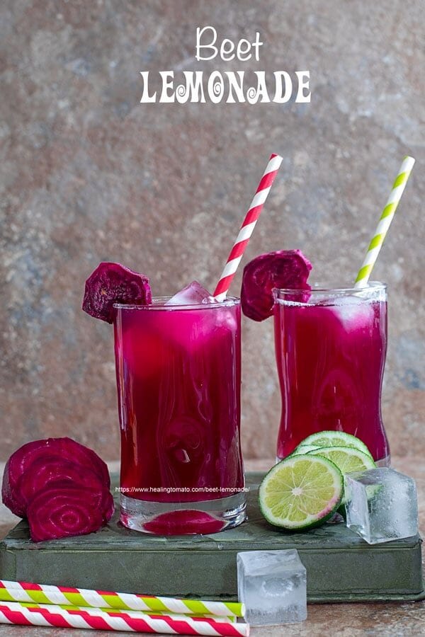 Front view of two small glasses filled with beet lemonade. Ice cubes inside, red, green paper straw to the side and a slice of beet lemonade for garnish