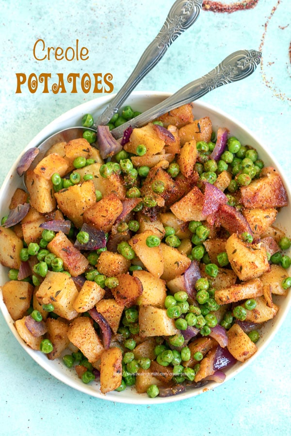 Top view of potatoes and peas on a white plate with two silver spoons on the top left side of the plate