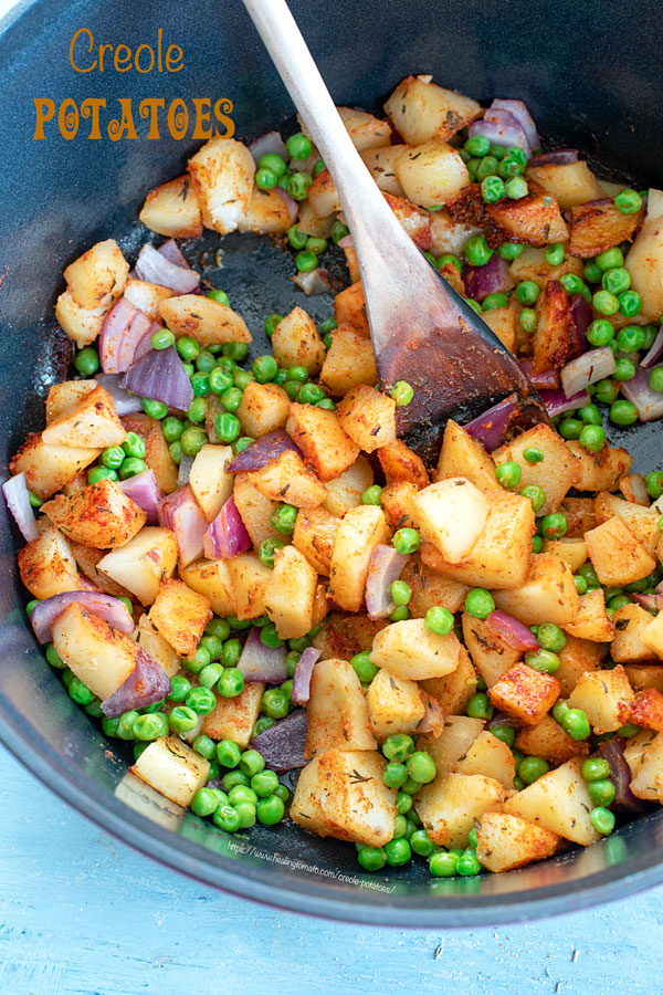 Top view of creole potatoes and peas in the Dutch oven with a wooden spoon