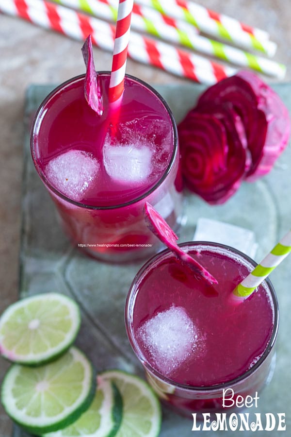 Top view of 2 small glasses filled with beet lemonade. Ice cubes inside, a red and green paper straw to the side and a slice of beet lemonade for garnish