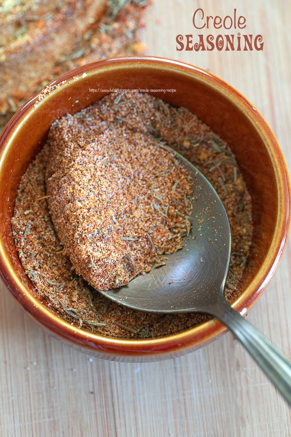Closeup view of a small brown bowl filled with creole seasoning with a spoon in the bowl.