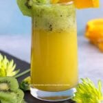 Front view of a glass filled with orange spritzer an topped with muddled kiwi