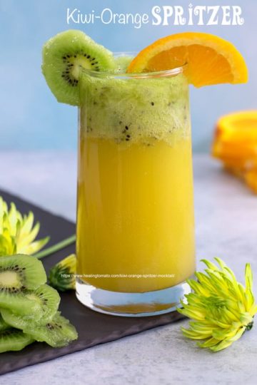 Front view of a glass filled with orange spritzer an topped with muddled kiwi