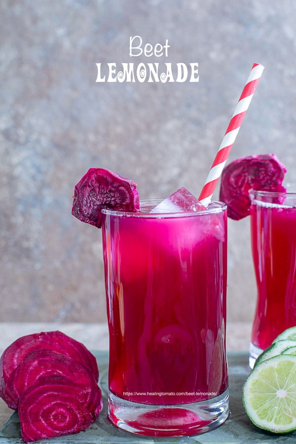 Front view of a small glass filled with beet lemonade. Ice cubes inside, a red paper straw to the side and a slice of beet lemonade for garnish