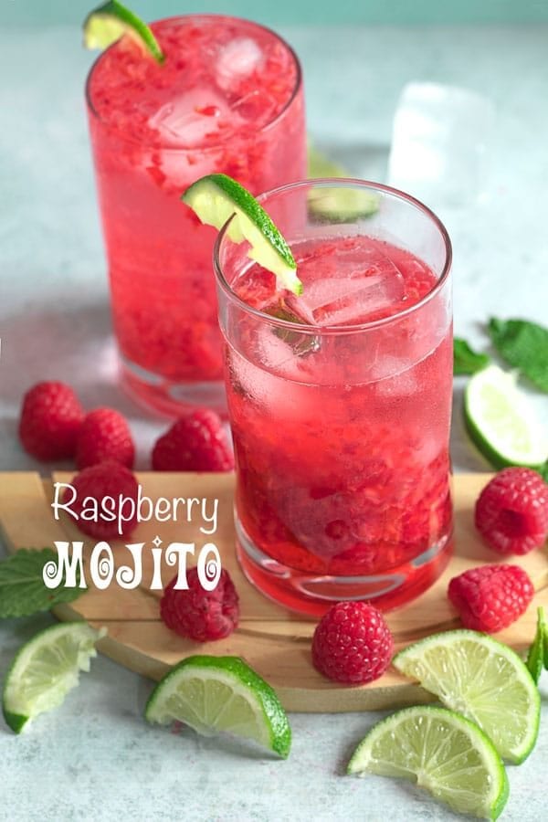 Front view of a glass filled with raspberry mojito recipe and surrounded by raspberries and lime