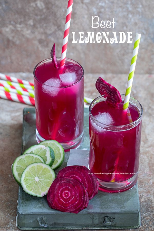 Front view of two small glasses filled with beet lemonade. Ice cubes inside, red, green paper straw to the side and a slice of beet lemonade for garnish