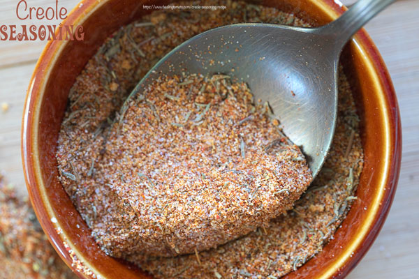 Closeup view of a small brown bowl filled with creole seasoning with a spoon in the bowl.