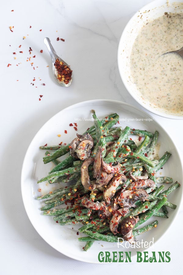 Top view of green beans and mushrooms in a white plate with red pepper flakes for garnish