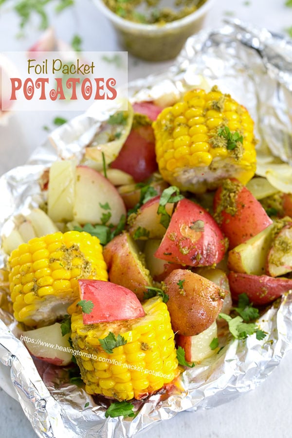 Top view of potatoes and mini corn on the cob inside an aluminium wrap