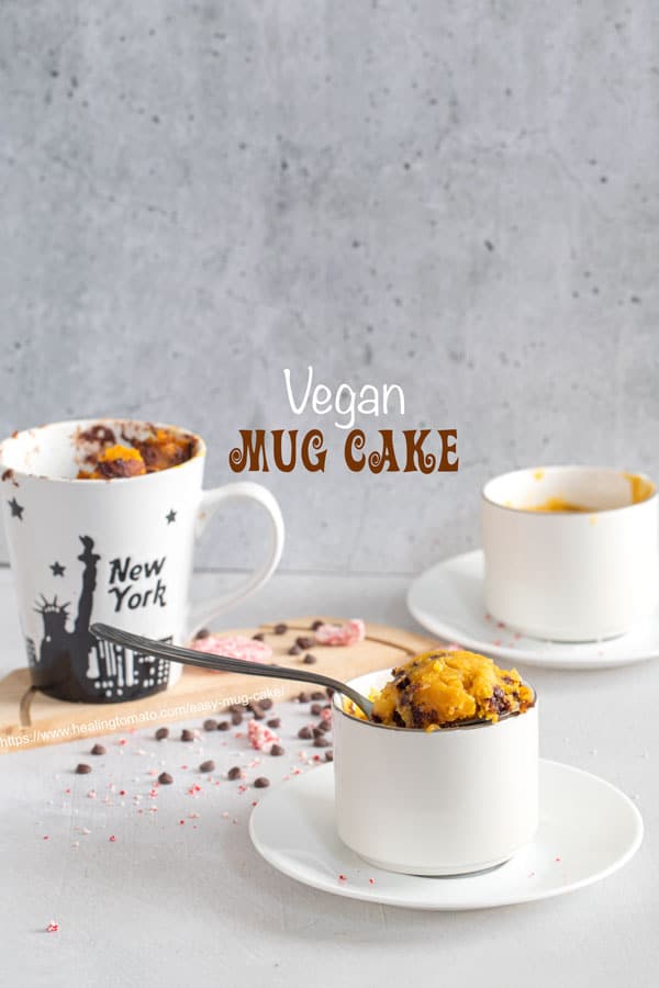 front view of 3 a mug filled with an easy mug cake. Two more mugs in the background and chocolate chips strewn around the mugs
