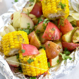 Top view of potatoes and mini corn on the cob inside an aluminium wrap