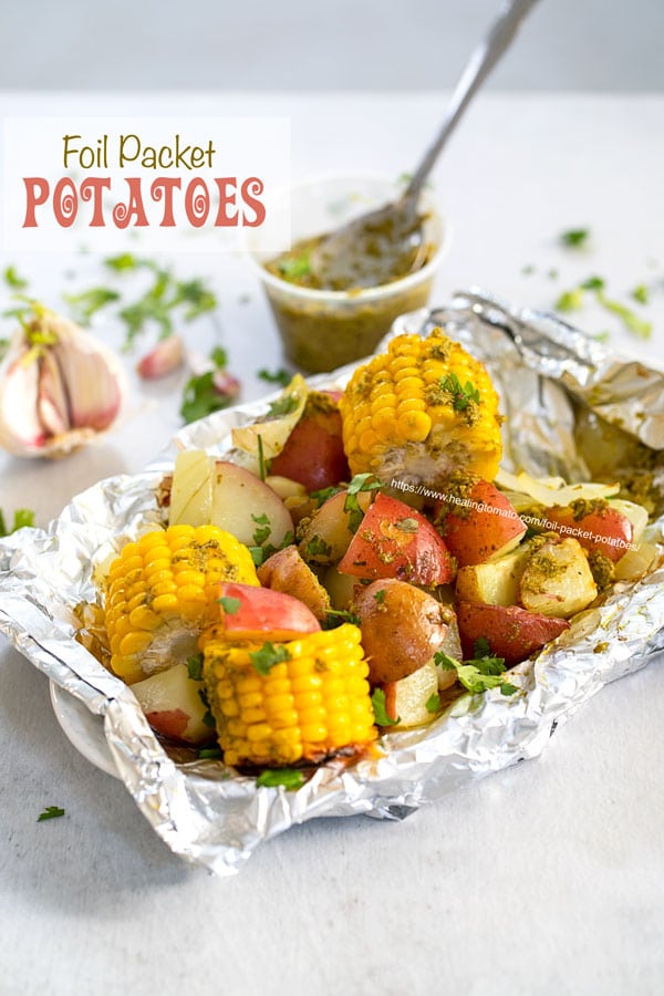 Angle view of potatoes and mini corn on the cob inside an aluminium wrap