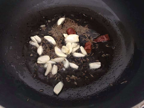top view of garlic, cumin, dry chili in oil in a frying pan
