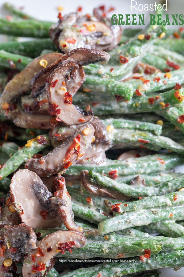 Closeup view of green beans and mushrooms in a white plate with red pepper flakes for garnish