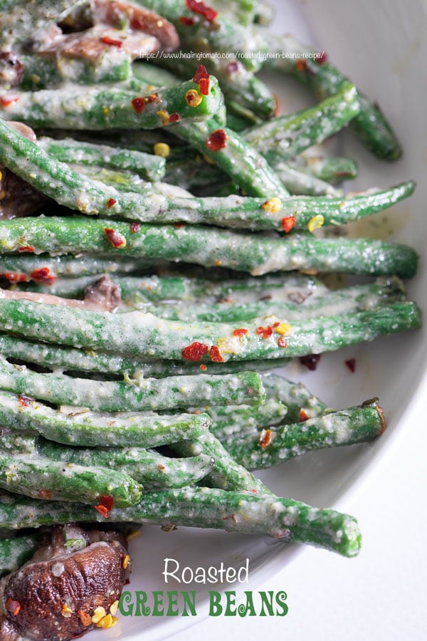 Closeup view of green beans and mushrooms in a white plate with red pepper flakes for garnish