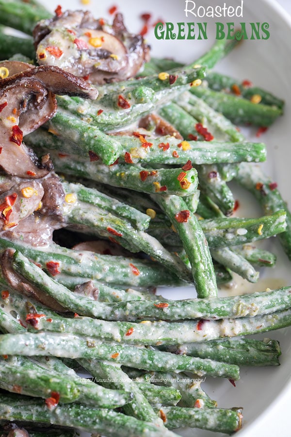 Closeup view of green beans and mushrooms in a white plate with red pepper flakes for garnish