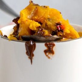 closeup view of a spoon filled with pumpkin and chocolate placed on the rim of a mug