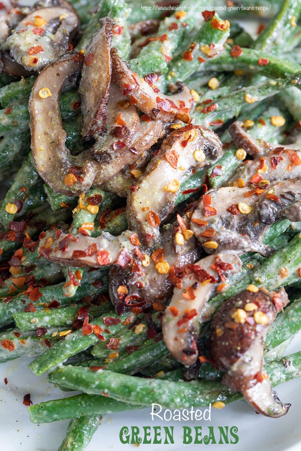 Closeup view of green beans and mushrooms in a white plate with red pepper flakes for garnish