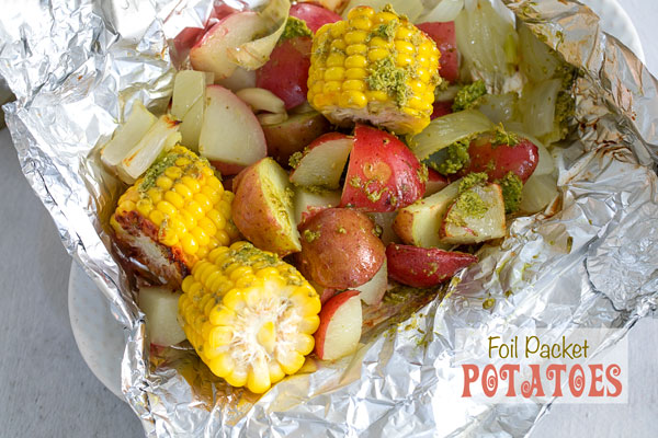 Closeup view of potatoes and mini corn on the cob inside an aluminium wrap