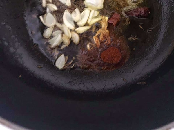 top view of garlic, red chili powder, dry chili in oil in a frying pan