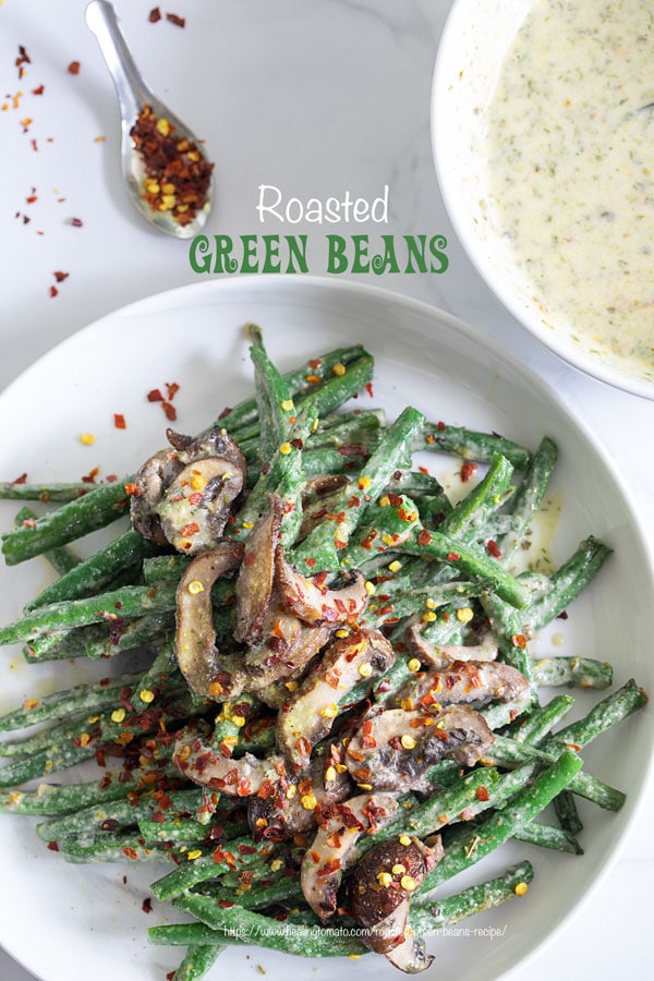 Top view of green beans and mushrooms in a white plate with red pepper flakes for garnish