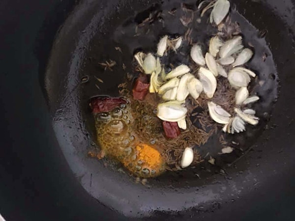 top view of garlic, turmeric, dry chili in oil in a frying pan