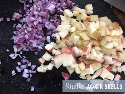 On a black chopping board, there are diced red onions on the left and diced apples on the right