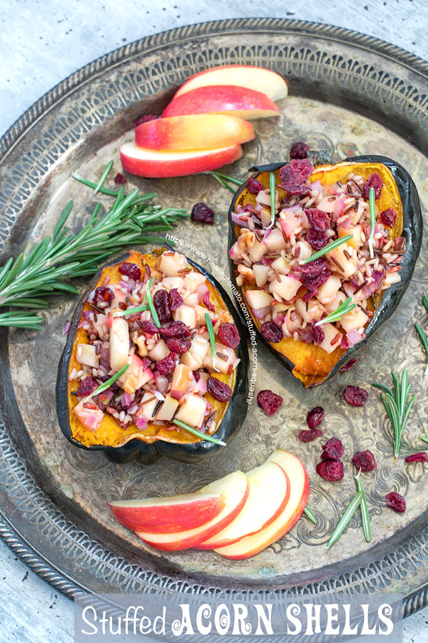 Top view of 2 stuffed acorn squash on a round grey serving tray with apple slices, rosemary sprigs and dried cranberries for garnish