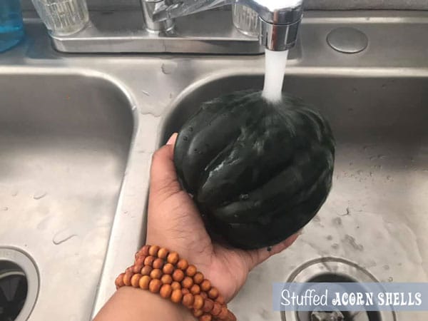 An acorn squash being held under a tap with running water