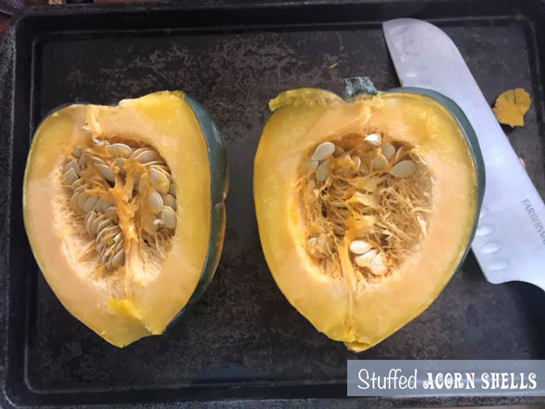 Acorn squash cut into half and placed on a baking tray with a long knife on the side