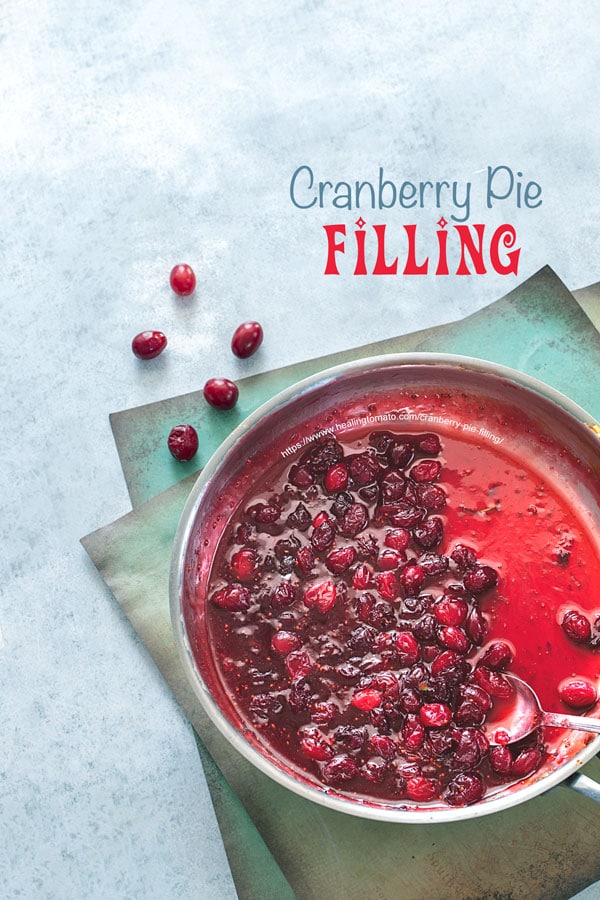 Top view of a stainless steel pan filled with cranberry pie filling on a blue background with a few cranberries on the side