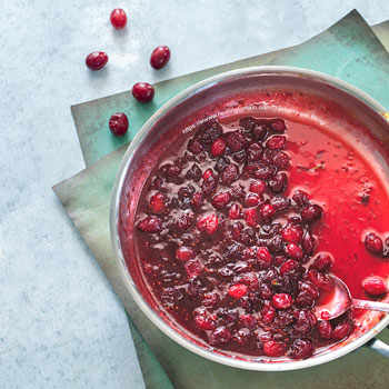 top view of vegan cranberry pie filling in a stainless steel pan with a spoon in it.