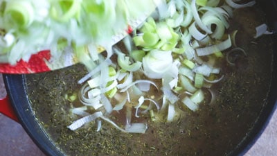 A colorful plate filled with chopped leek.  The chopped leek are being poured into the water in Dutch oven