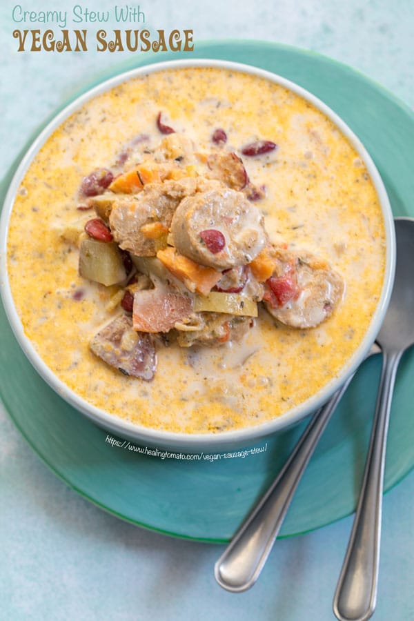 Top view of vegan sausage stew in a grey bowl on a turquoise plate with 2 spoons on the side