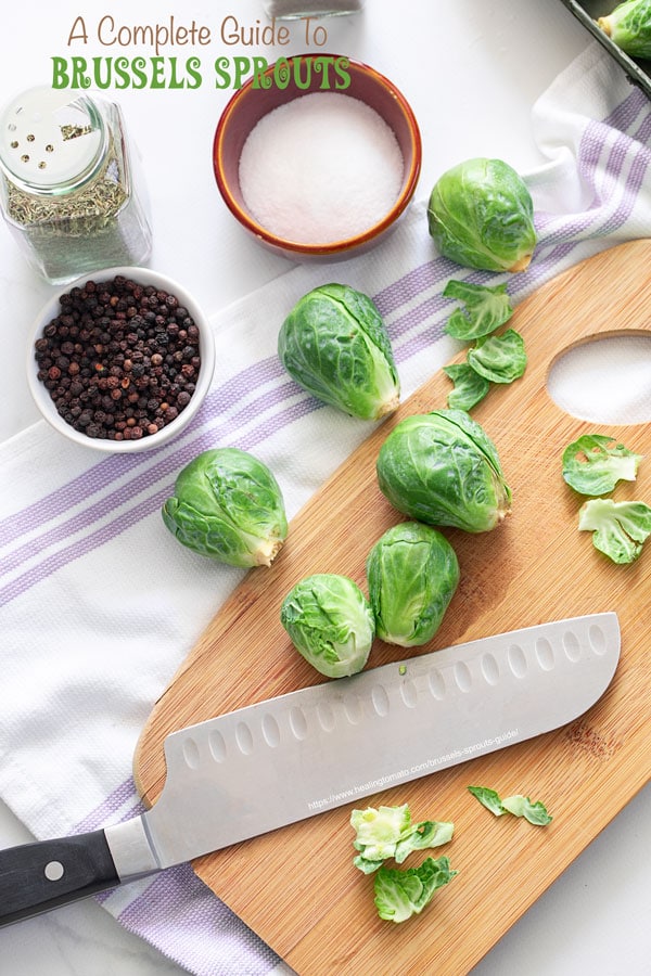 Top view of Brussels sprouts on a cutting board on cloth with a large cutting knife and seasonings around it.