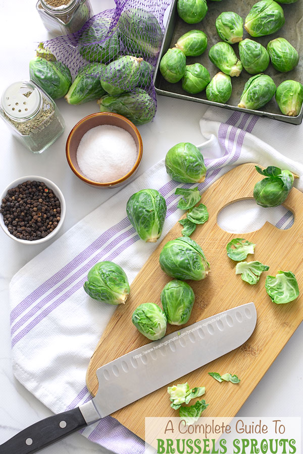 Top view of Brussels sprouts on a cutting board on cloth with a large cutting knife and seasonings around it.