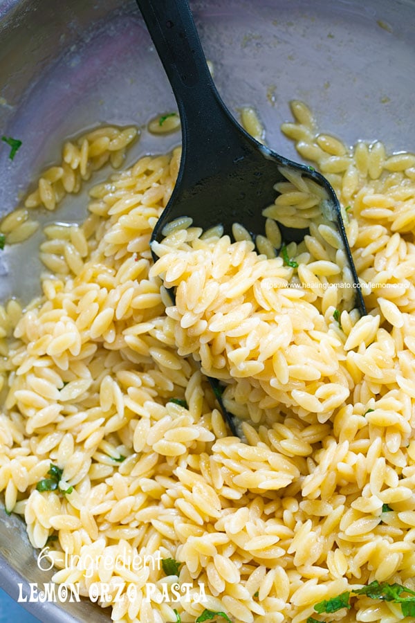 closeup view of lemon orzo pasta in a stainless steel pan with a black serving spoon