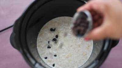 The author's hand are shown adding vegan chocolate chips into the crock-pot container