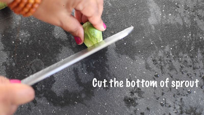 The author using a large kitchen knife to cut the bottom of the sprout