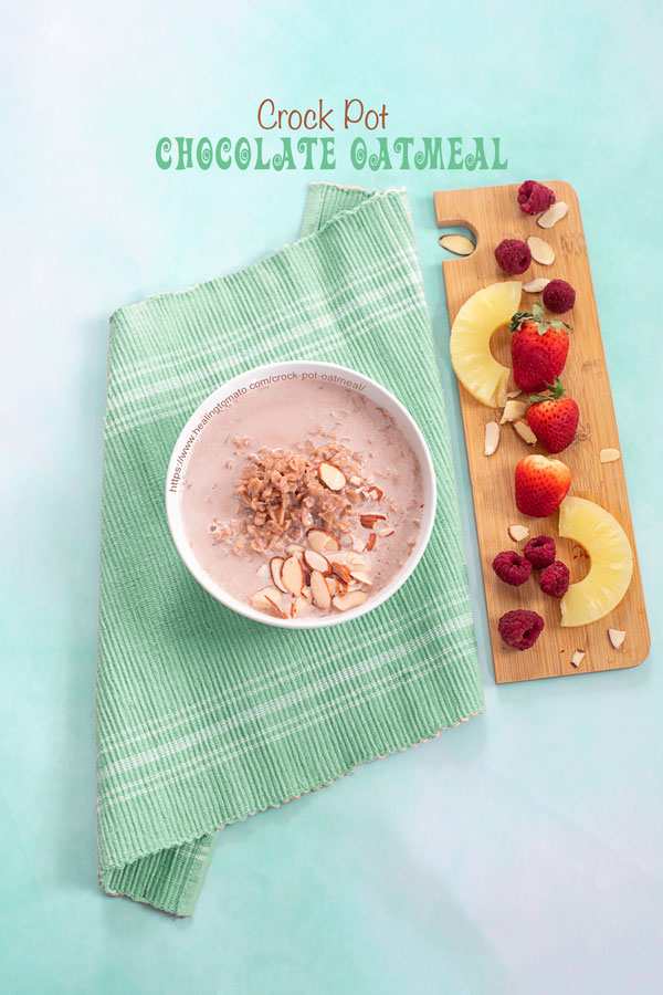 Top view of a white bowl filled with chocolate oatmeal. Bowl is on a green placemat with fruits on the side