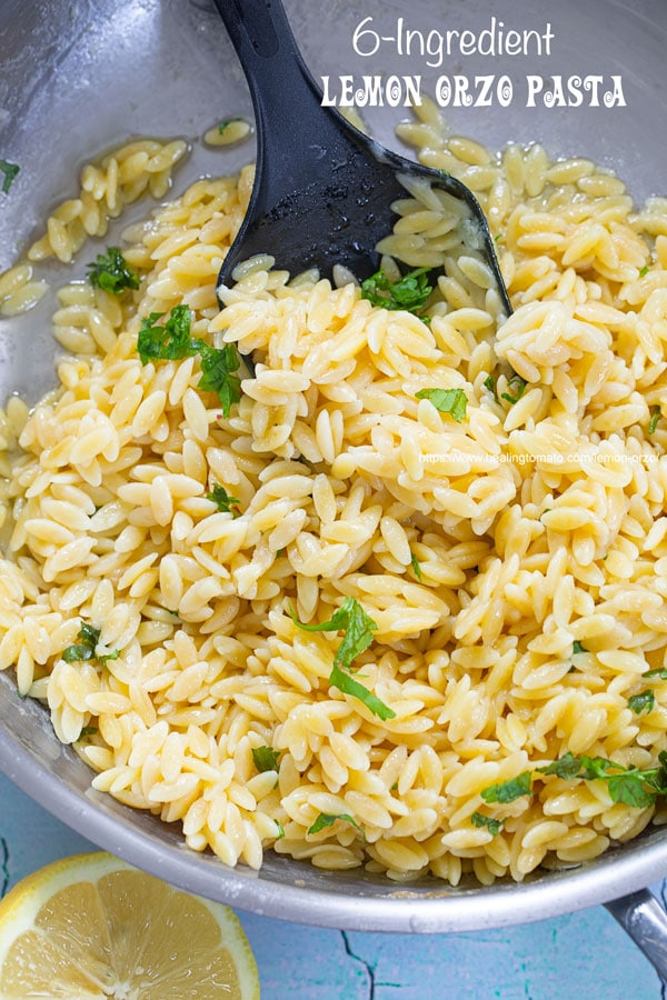 closeup view of lemon and orzo cooked in a stainless steel pan with a black serving spoon 