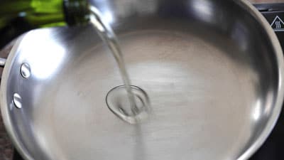 A green bottle pouring extra virgin olive oil to a stainless steel pan