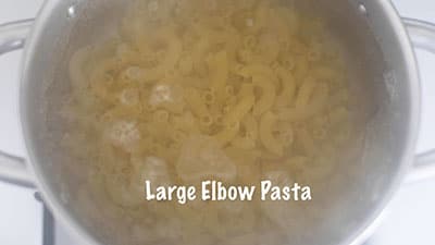 Large elbow pasta and water shown inside a stainless steel pan