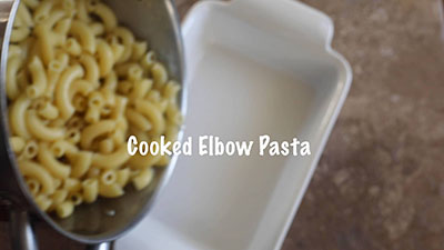 Cooked elbow macaroni being transferred to a white baking dish