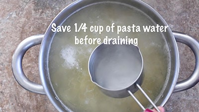 The author scooping out ¼ cup of water from the cooked pasta pan