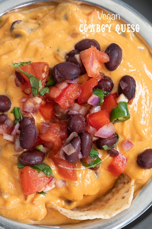 Top and closeup view of the vegan cowboy queso topped with black bean mixture. There is a tostitos scoop chip on the edge of the queso dip