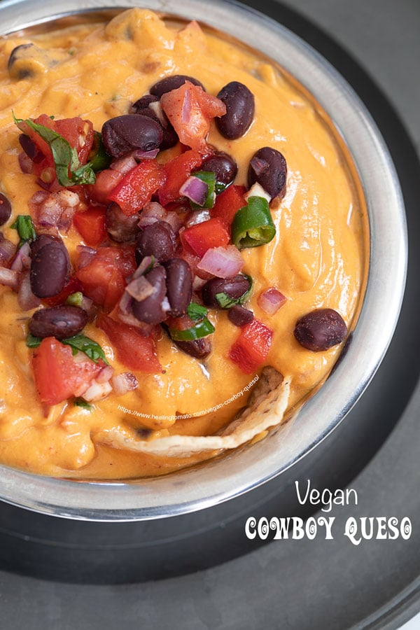 Top view of the vegan cowboy queso topped with black bean mixture. There is a tostitos scoop chip on the edge of the queso dip