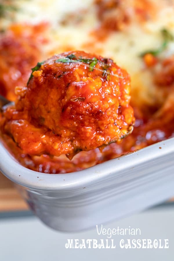 closeup view of a single plant-based meatball on a copper spoon with marinara and cheese on it.