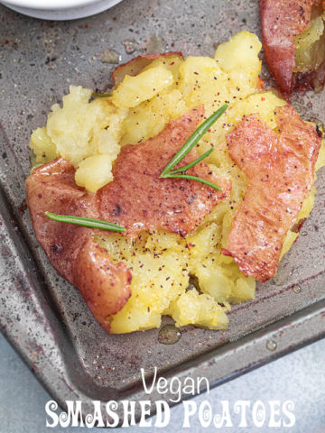 Closeup view of a single smashed baby potato garnished with rosemary sprigs, ground pepper and melted butter